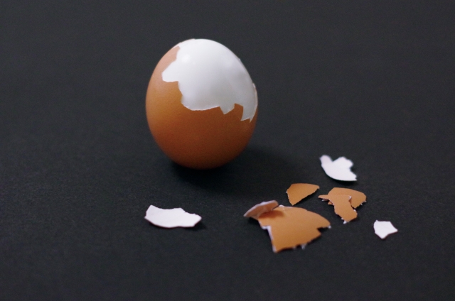  殻付きの剥きかけゆで卵・黒背景