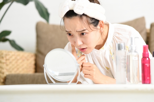 鏡を見ながら肌トラブルに悩む女性